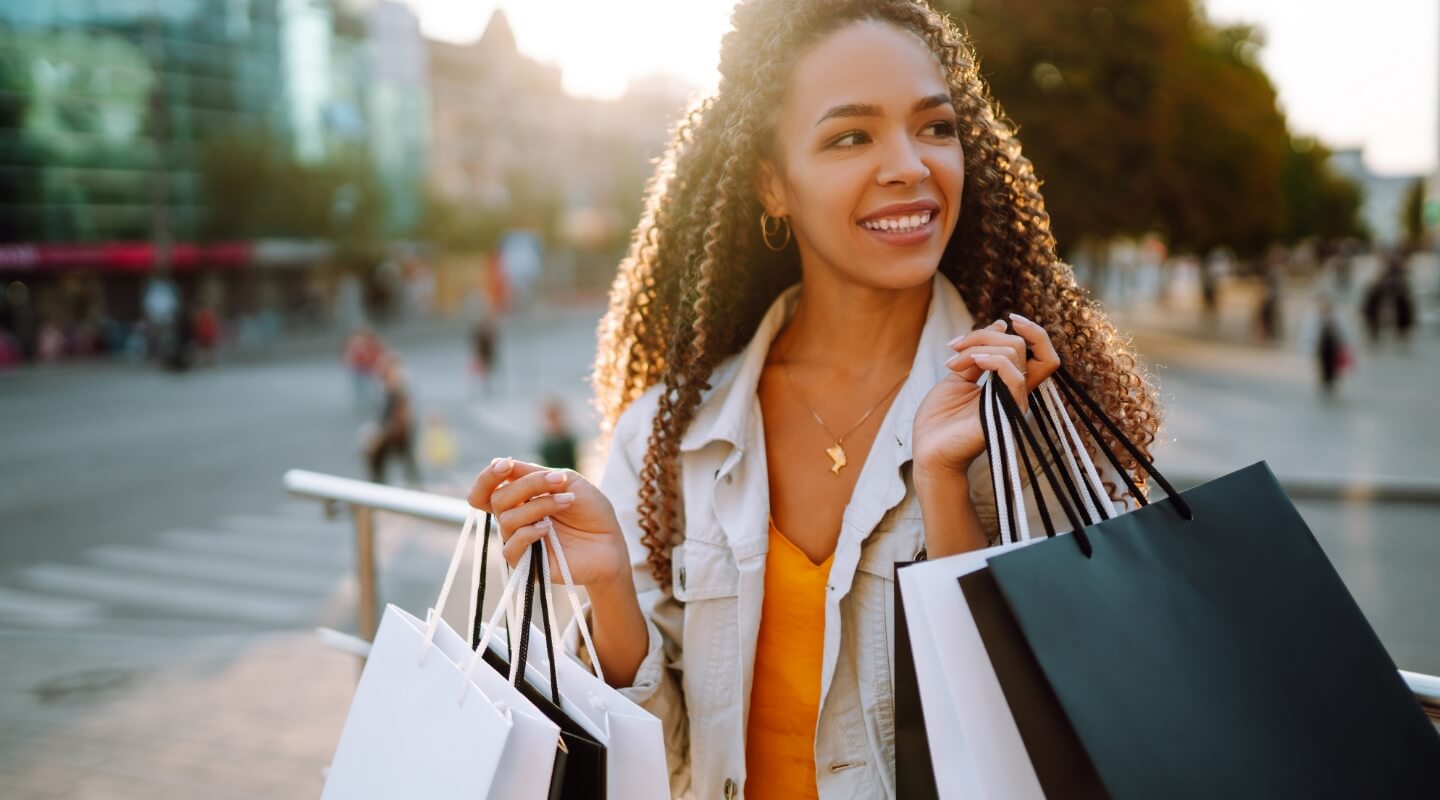a young woman carrying shopping bags outside and smiling